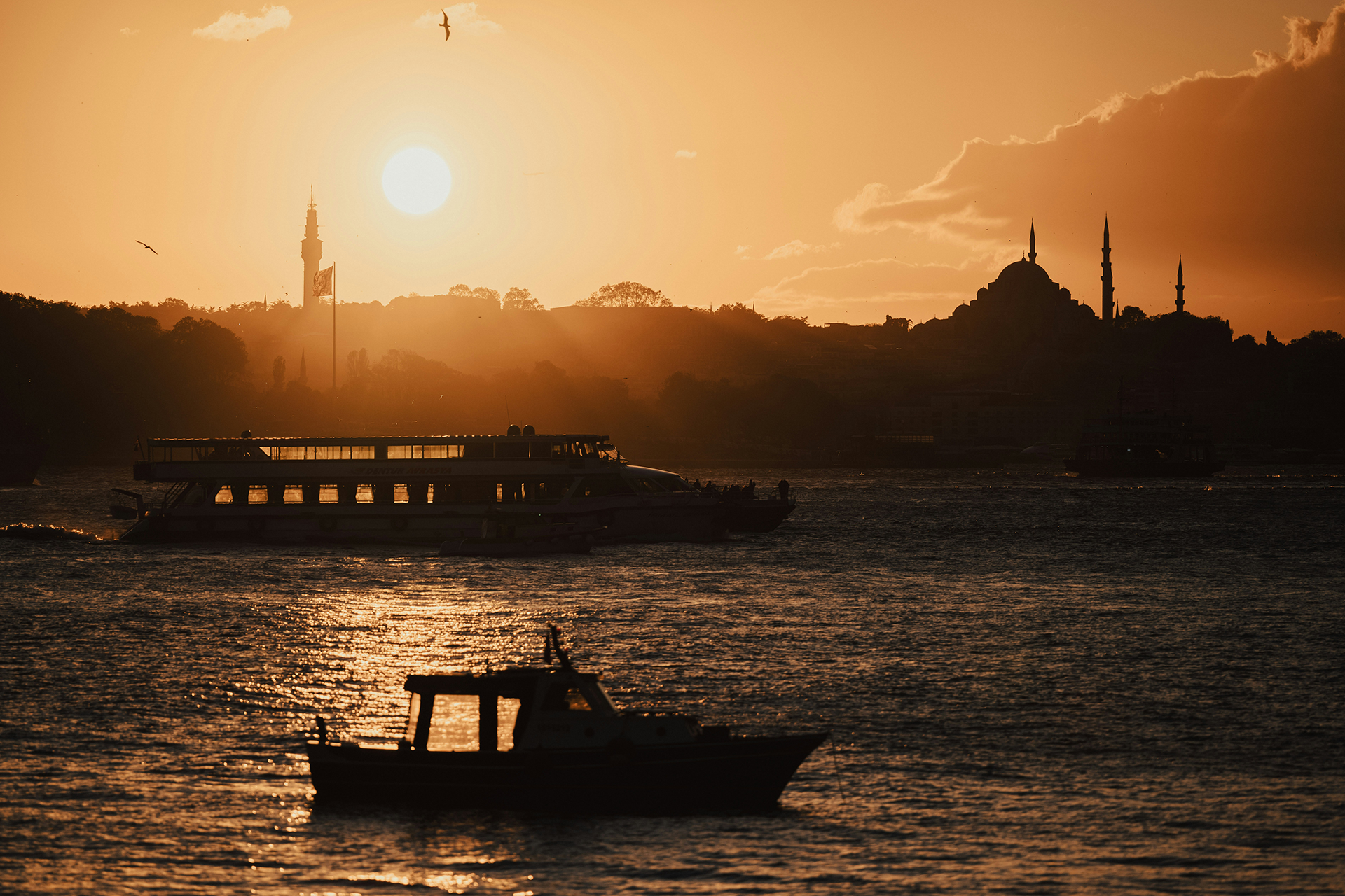 Boğaz üzerinde gün batımında İstanbul silueti, cami silueti ve sularda tekneler